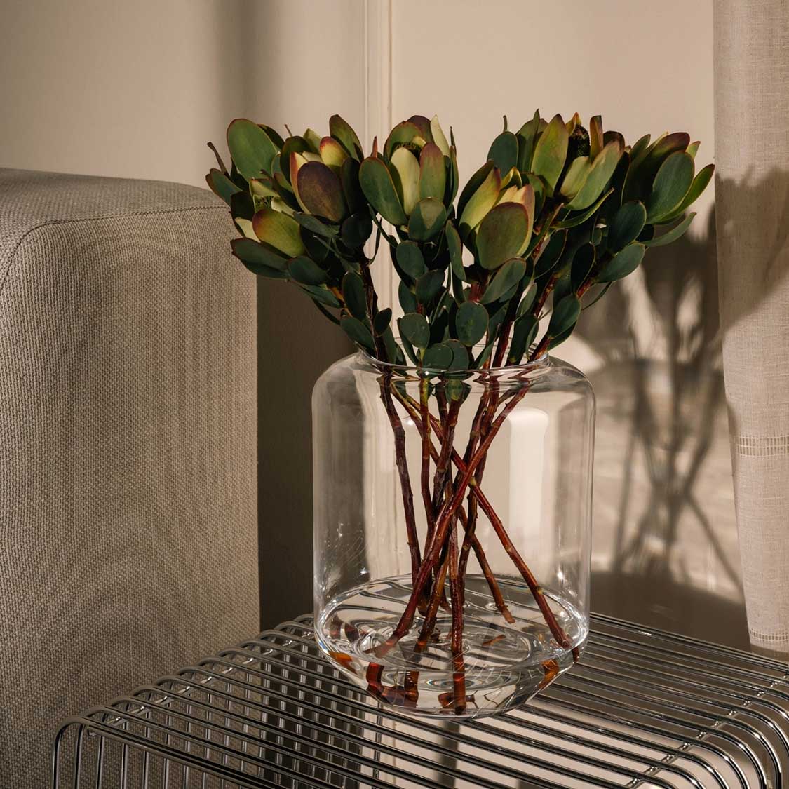 Windlicht MILANO mit grünen Blüten in Wohnraum auf gestreiftem Tisch