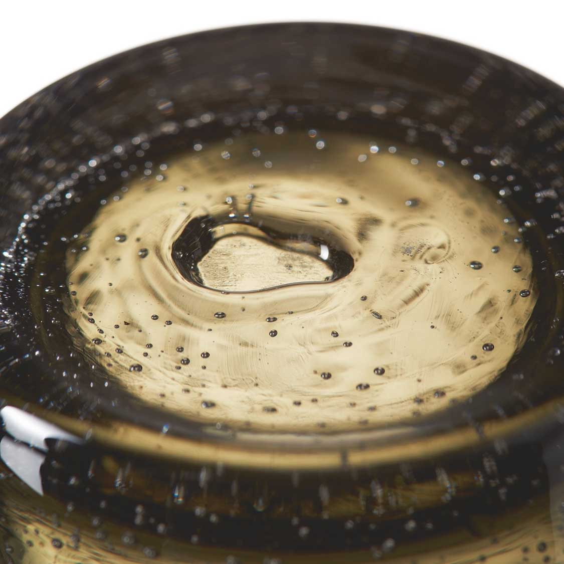 Dunkelgraues Glas von oben, gefüllt mit heller Flüssigkeit und Blasen
