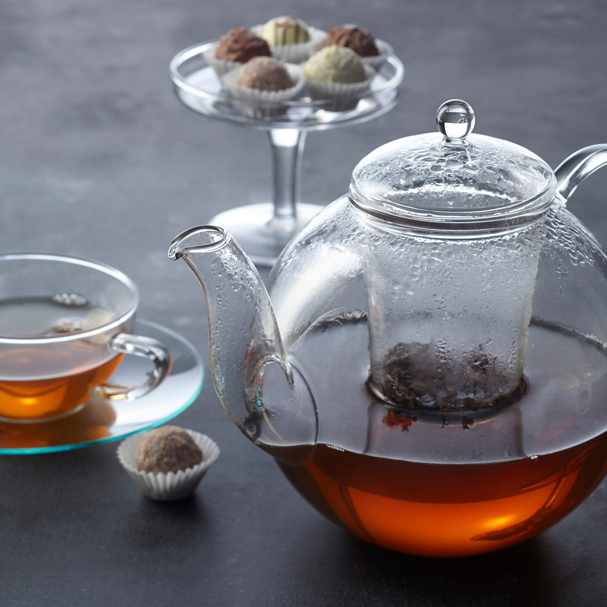 Teekanne ARMONIA mit Tee, Tasse und Pralinen auf Tisch