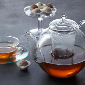 Teekanne ARMONIA mit Tee, Tasse und Pralinen auf Tisch