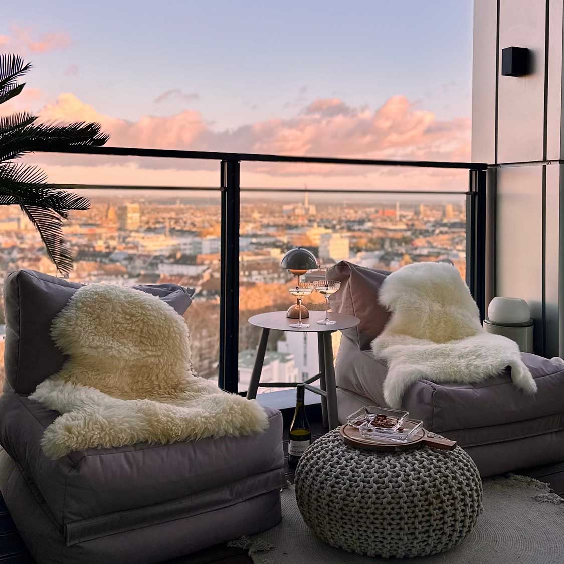 Luxuriöser Wohnraum mit Panoramablick auf Stadt, Sessel mit Fellauflagen, kleine Tische mit Dekoration