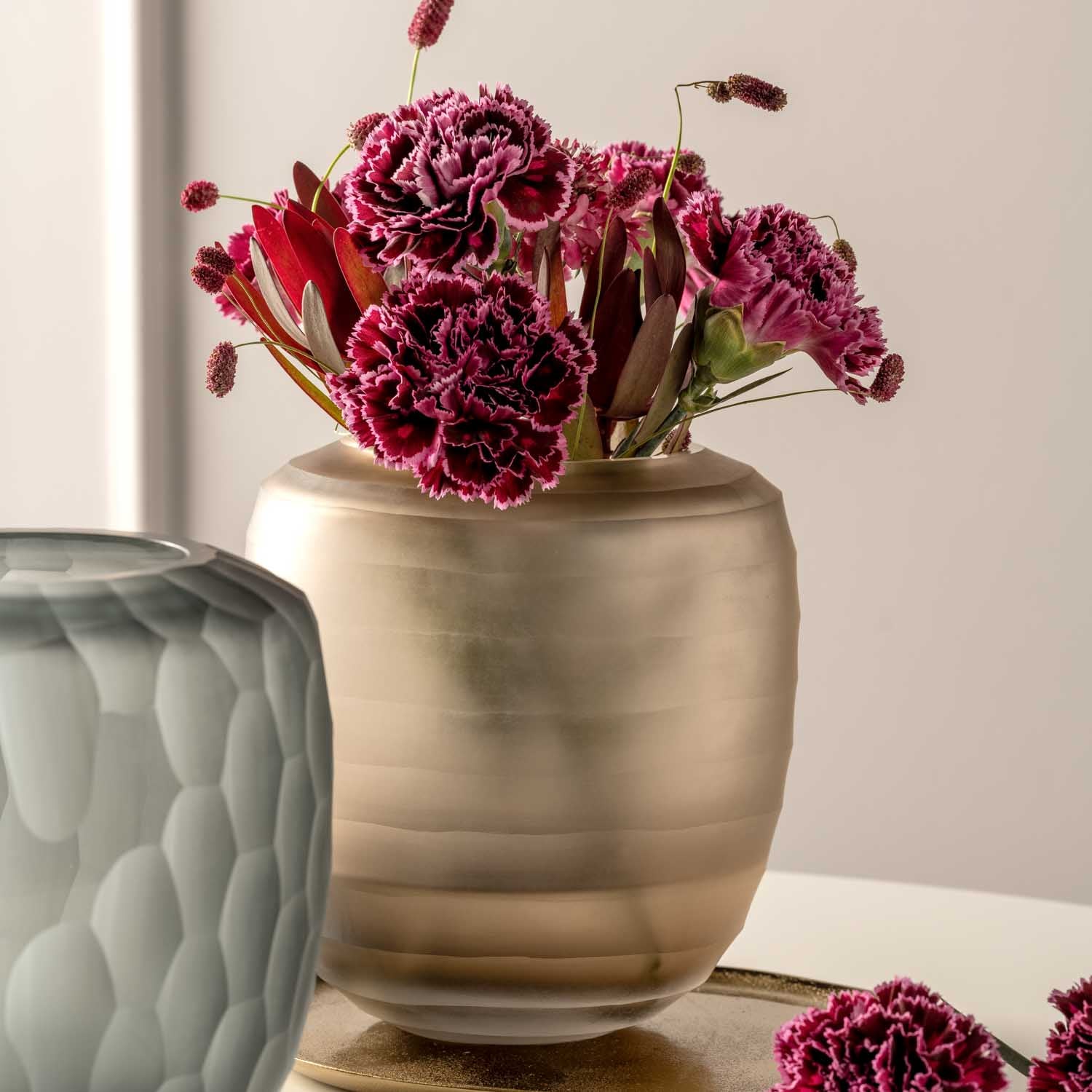 Vase BELLAGIO mit pinken Nelken auf Tisch neben grauem Objekt