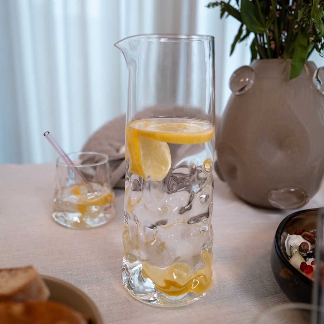 Karaffe SANO mit Zitronenwasser auf gedecktem Tisch