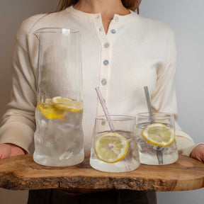 Frau mit drei Gläsern Zitronenwasser und Karaffe SANO auf Holztisch