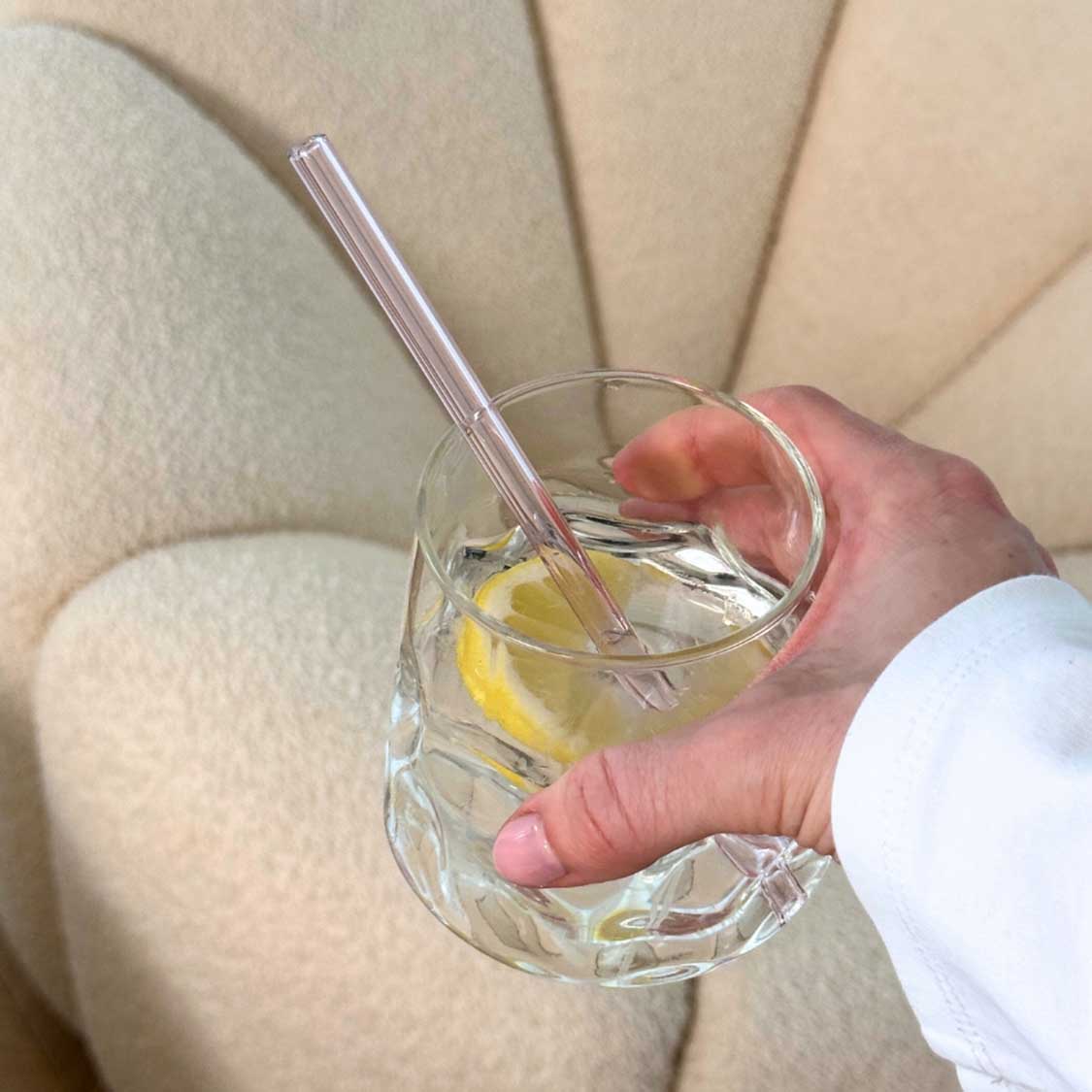 Person haelt Trinkglas SANO mit Zitronenscheibe und Strohhalm in Hand