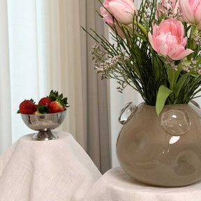 Vase HAZEL mit rosa Blüten und Gräsern, daneben Schale mit Erdbeeren auf Tuch