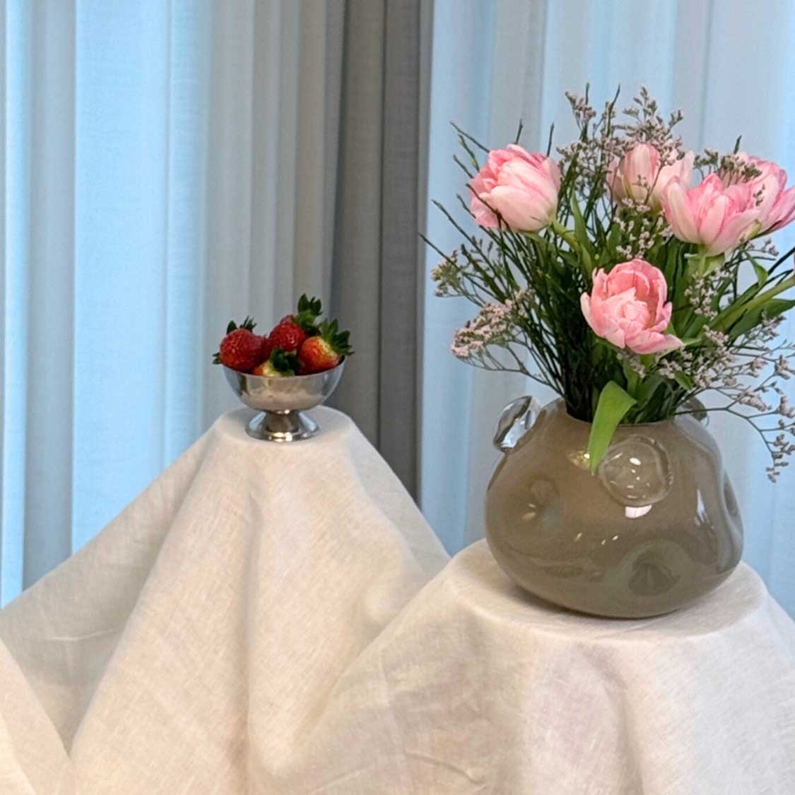 Vase HAZEL mit rosa Blüten auf gedecktem Tisch neben Schale mit Beeren