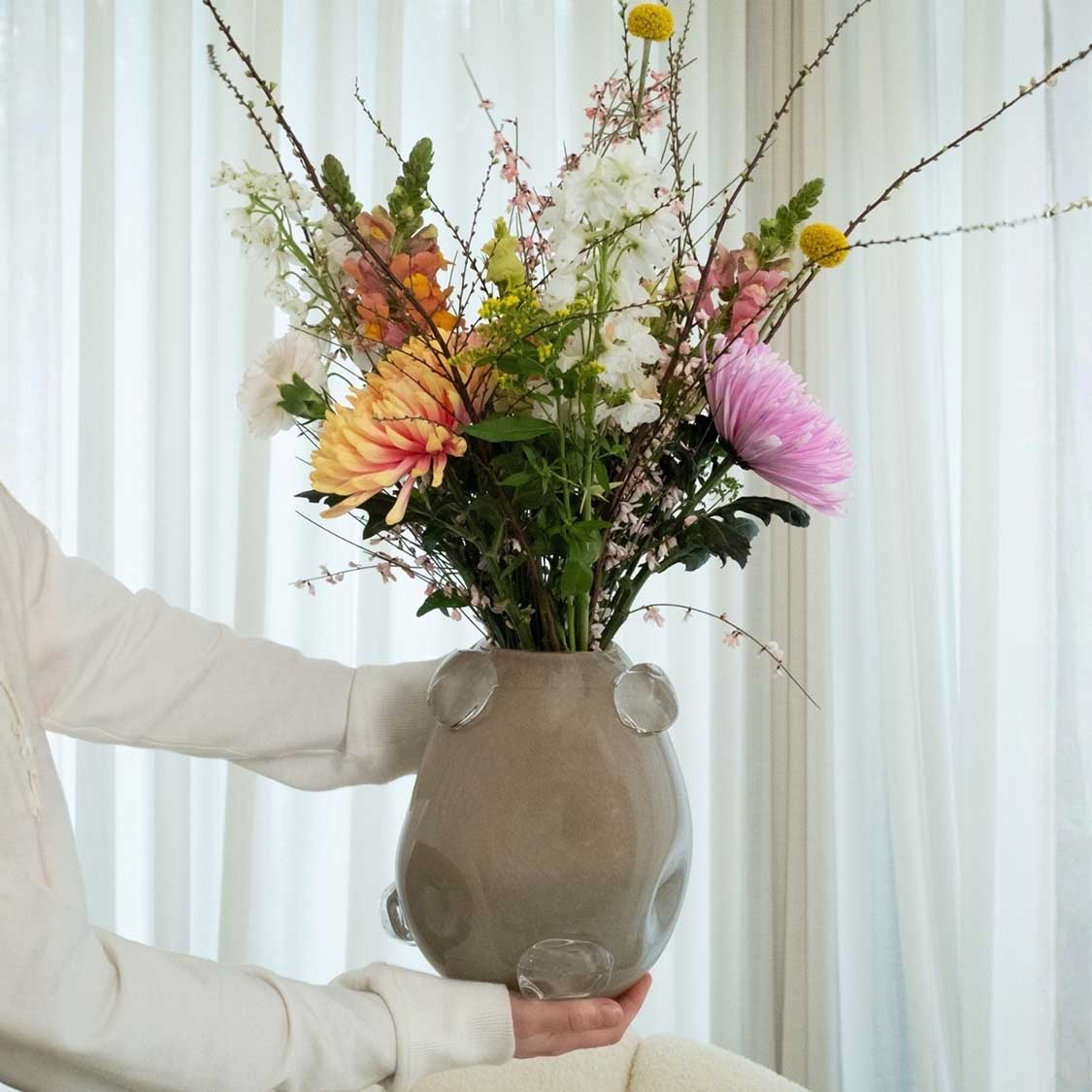 Vase HAZEL 25 cm beige mit buntem Blumenstrauß, von Person in heller Kleidung gehalten