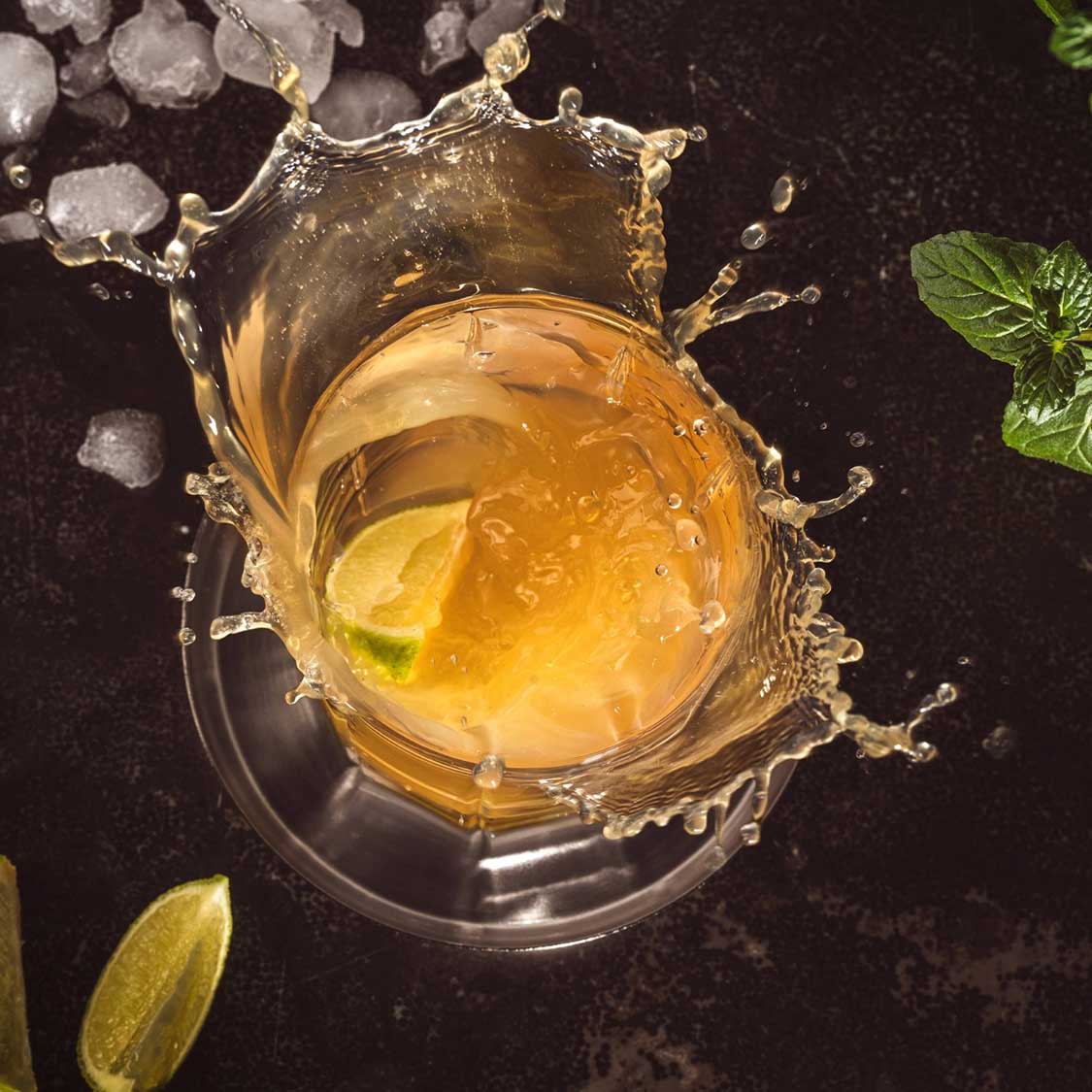 Whiskyglas mit Whiskey, Eiswürfeln und Limettenscheibe, dynamische Spritzwasserbewegung