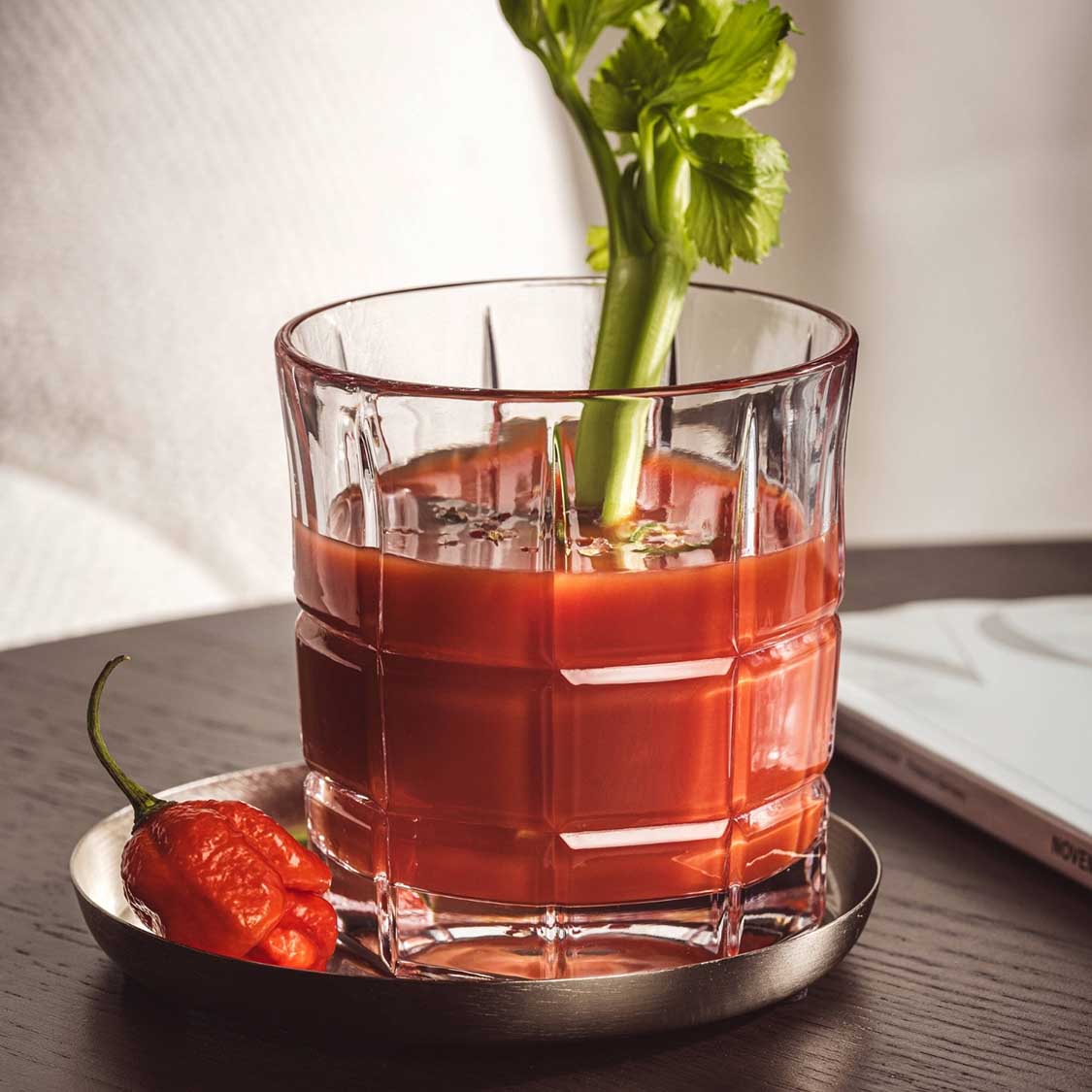 Whiskyglas mit rotem Getränk, Eiswürfeln und Selleriegarnitur auf Untersetzer