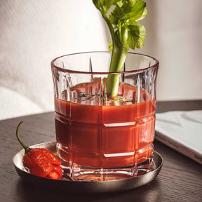 Whiskyglas mit rotem Getränk, Eiswürfeln und Selleriegarnitur auf Untersetzer