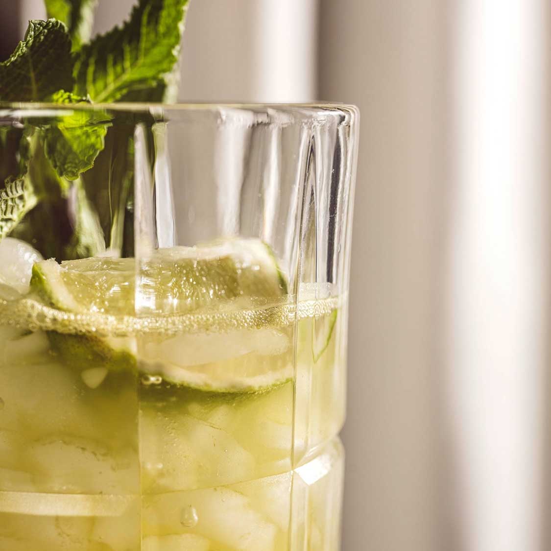 Longdrinkglas SPIRITII NOVA mit Zitronenscheibe und Minze in gelblicher Flüssigkeit