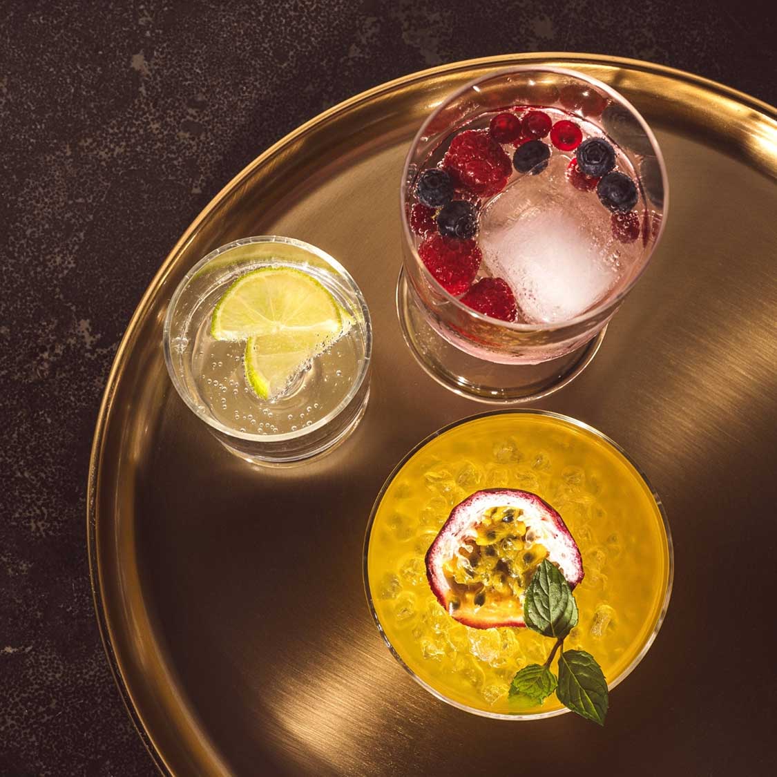 Kelchgläser mit farbigen Cocktails auf goldenem Tablett