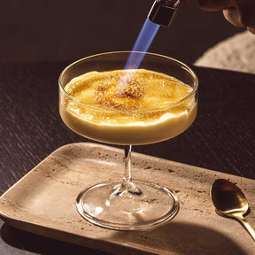 Schale auf Fuß BASSO gefüllt mit goldenem Cocktail, Feuerzangenbowle wird entzündet