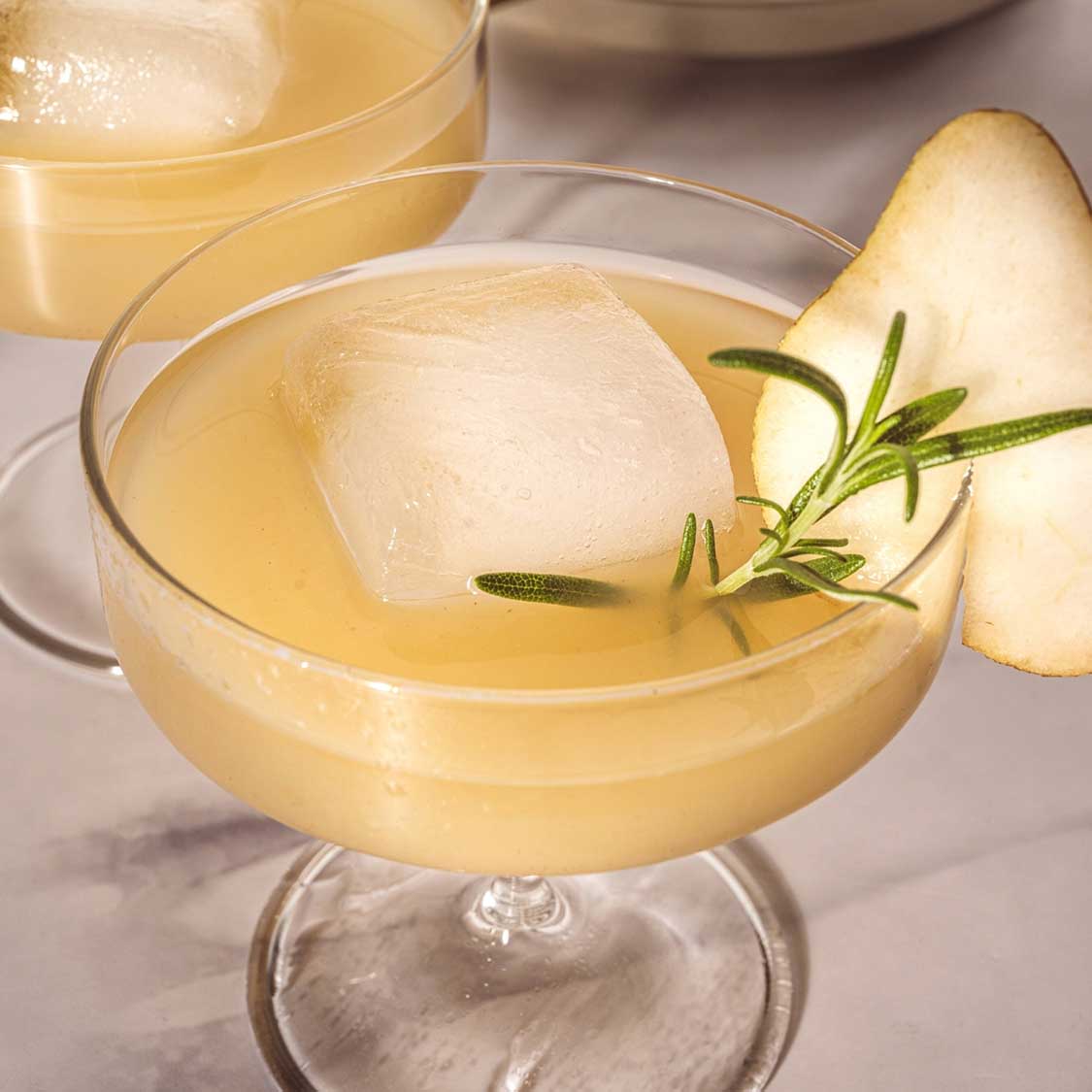 Schale auf Fuß BASSO mit Cocktail, Eiswürfel, Apfelscheibe und Rosmarinzweig gefüllt