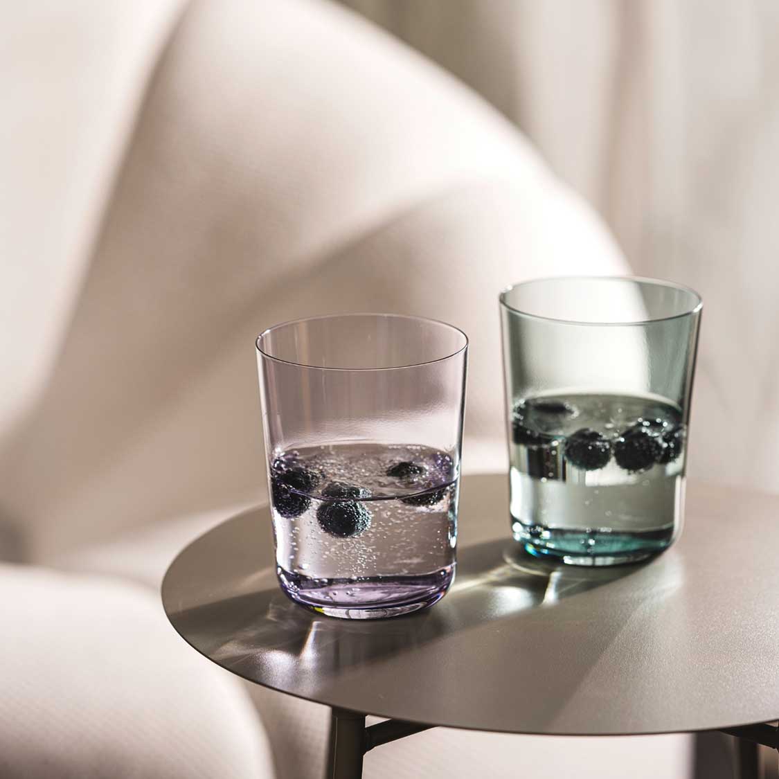 Zwei Trinkgläser LEGGERO mit Wasser und Eiswürfeln auf rundem Tisch, helles Interieur