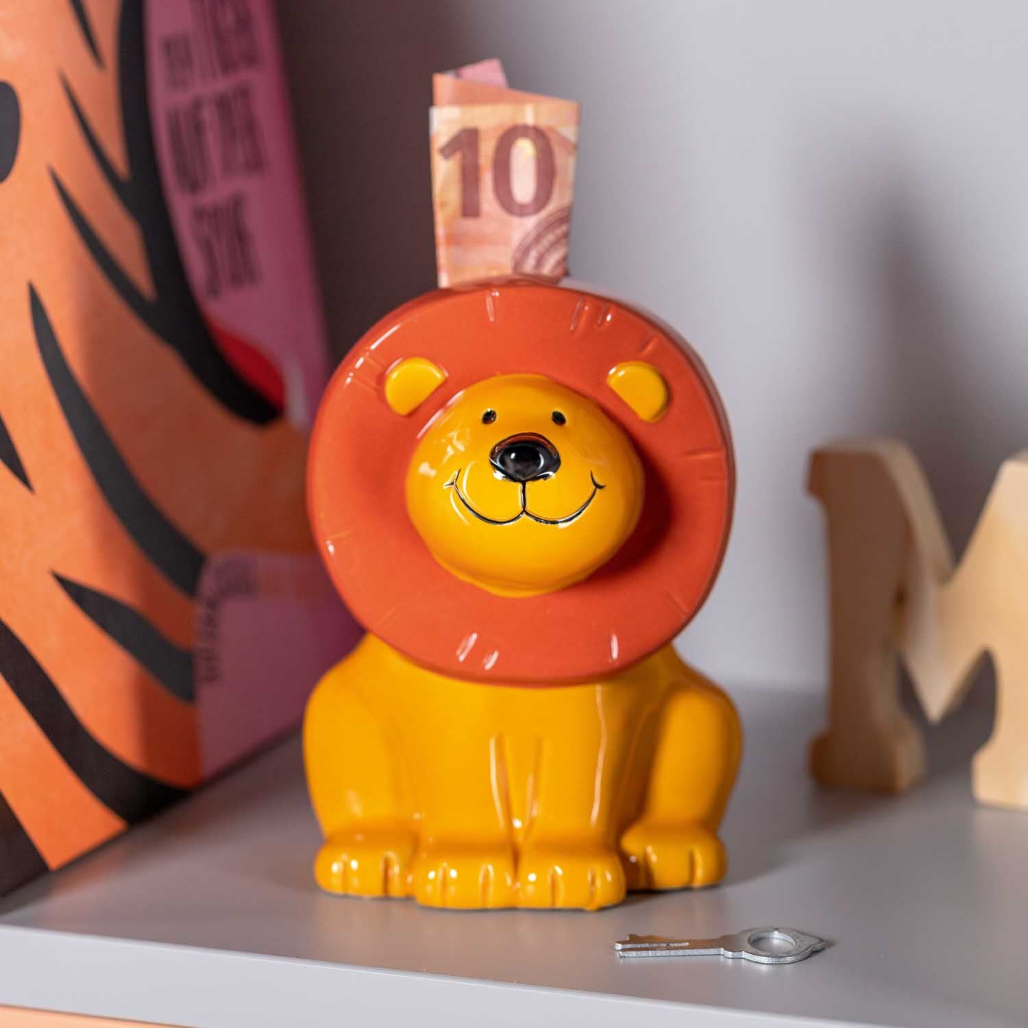 Spardose BAMBINI Löwe mit Geldschein auf orangefarbenem Hintergrund