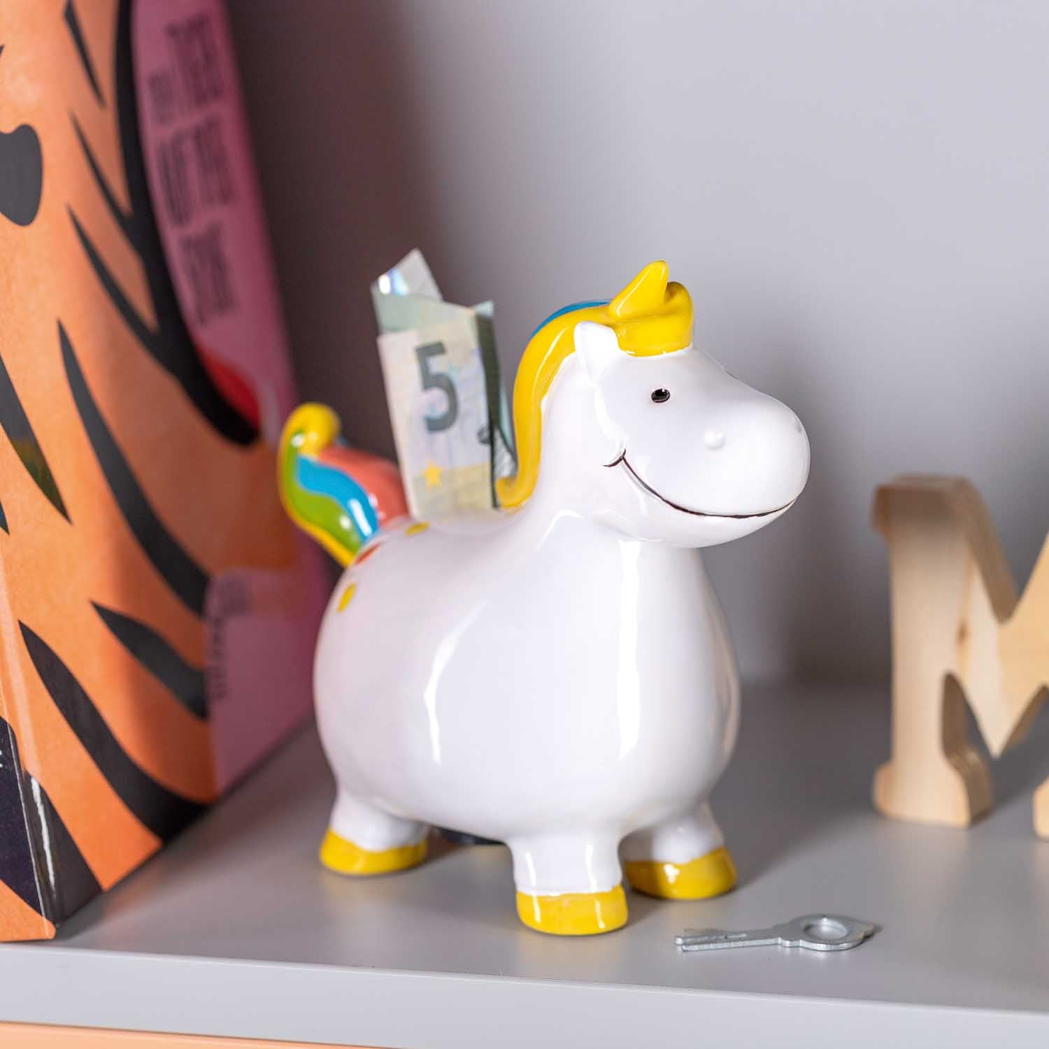 Spardose BAMBINI Einhorn mit gelben Akzenten auf Regal zwischen Deko-Objekten