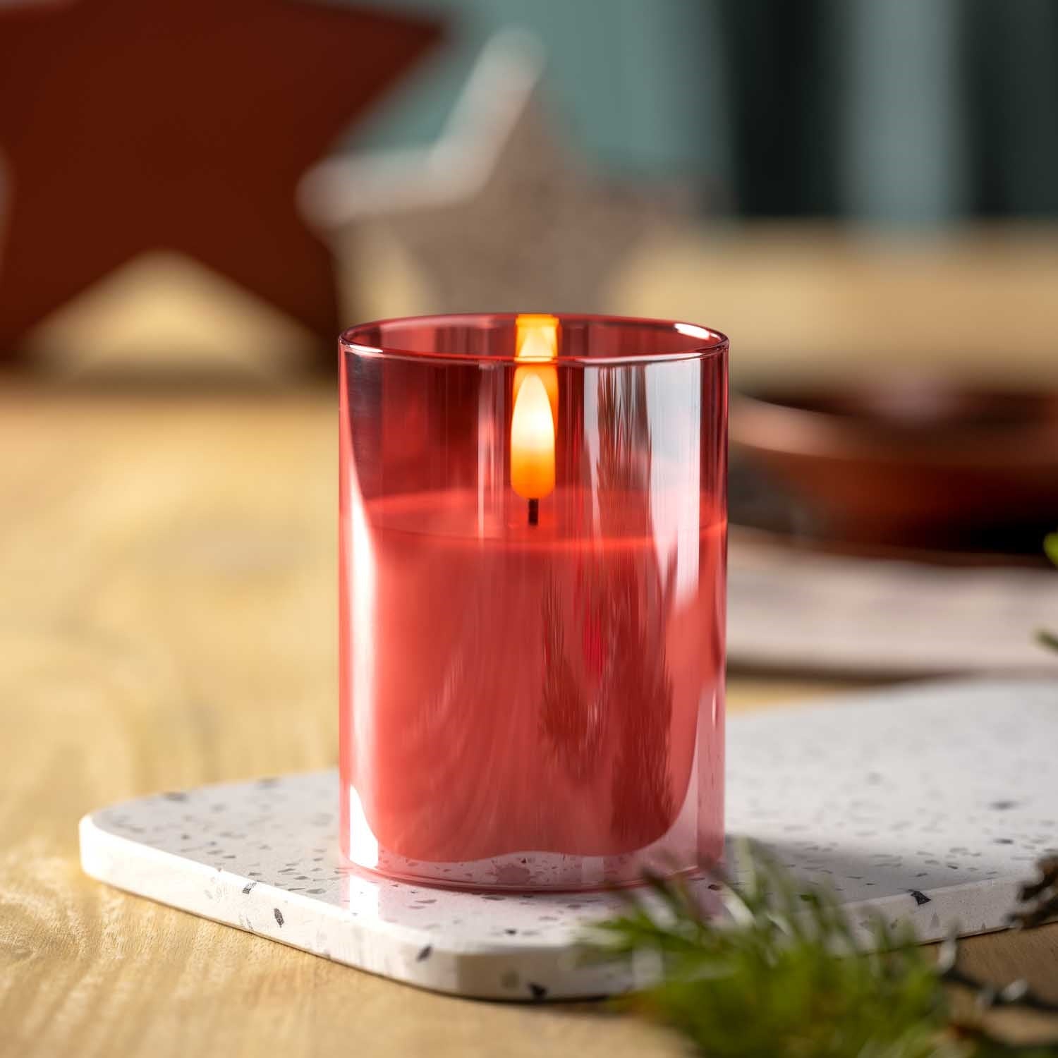 LED Kerze rot auf Marmor-Untersetzer, brennend auf Holztisch