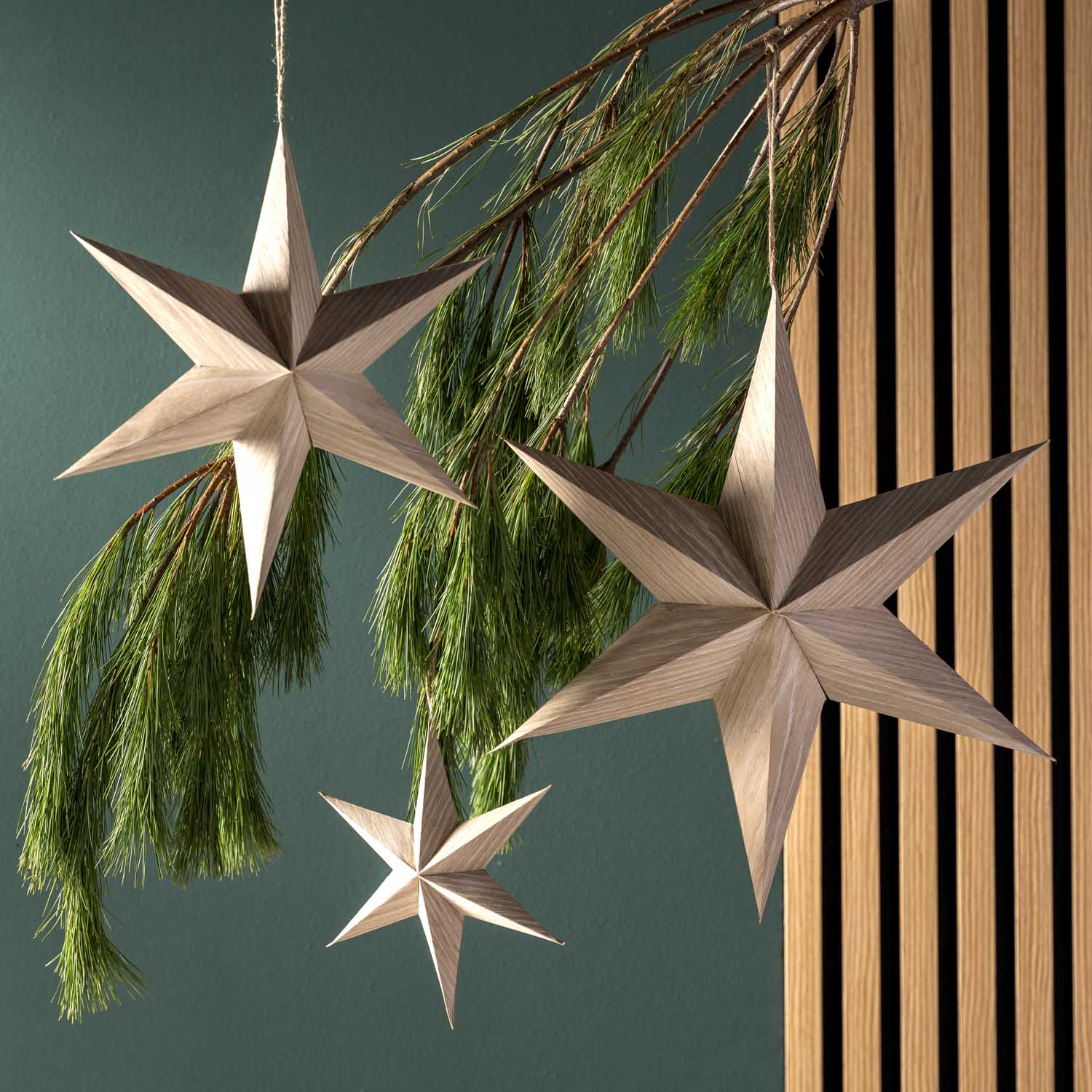 Sternhänger aus Holzfurnier in Beige, an Tannenzweigen hängend, vor grüner Wand und Holzpaneelen