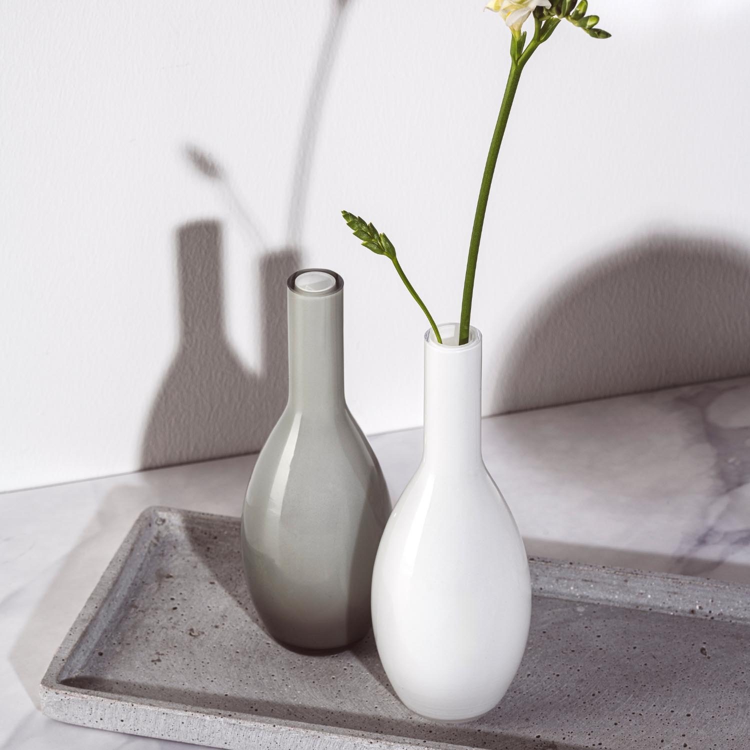 Vase BEAUTY 18 cm weiß mit Blumen auf Betonablage, daneben Glasflasche