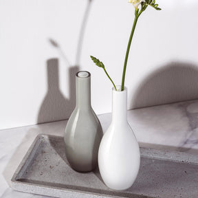 Vase BEAUTY 18 cm weiß mit Blumen auf Betonablage, daneben Glasflasche