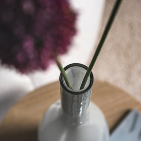 Vase BEAUTY mit grünen Stielen und lila Blüte in Wohnraum auf Holztisch