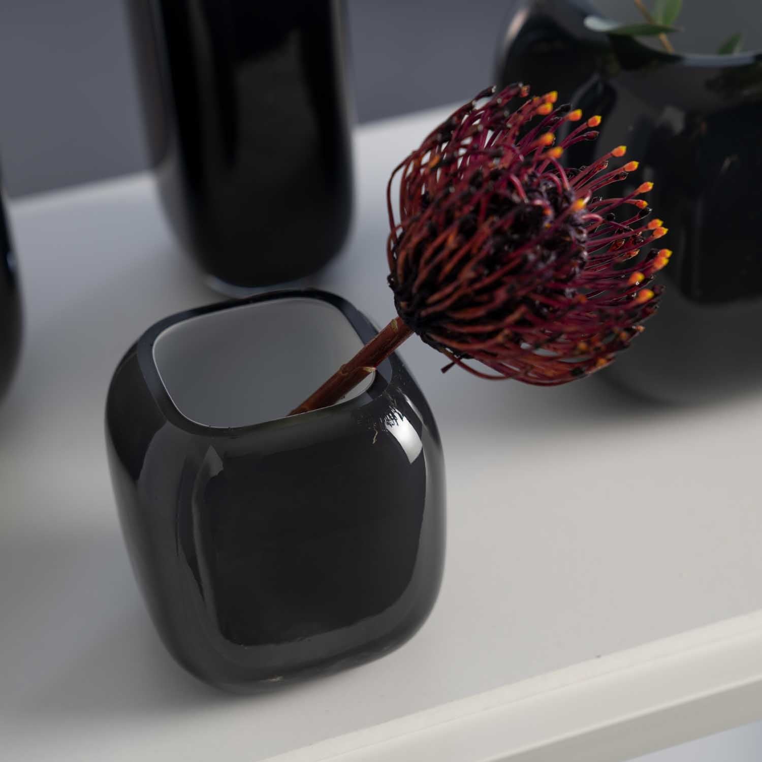 Vase MILANO mit roter Blüte auf weißer Oberfläche neben weiteren Vasen