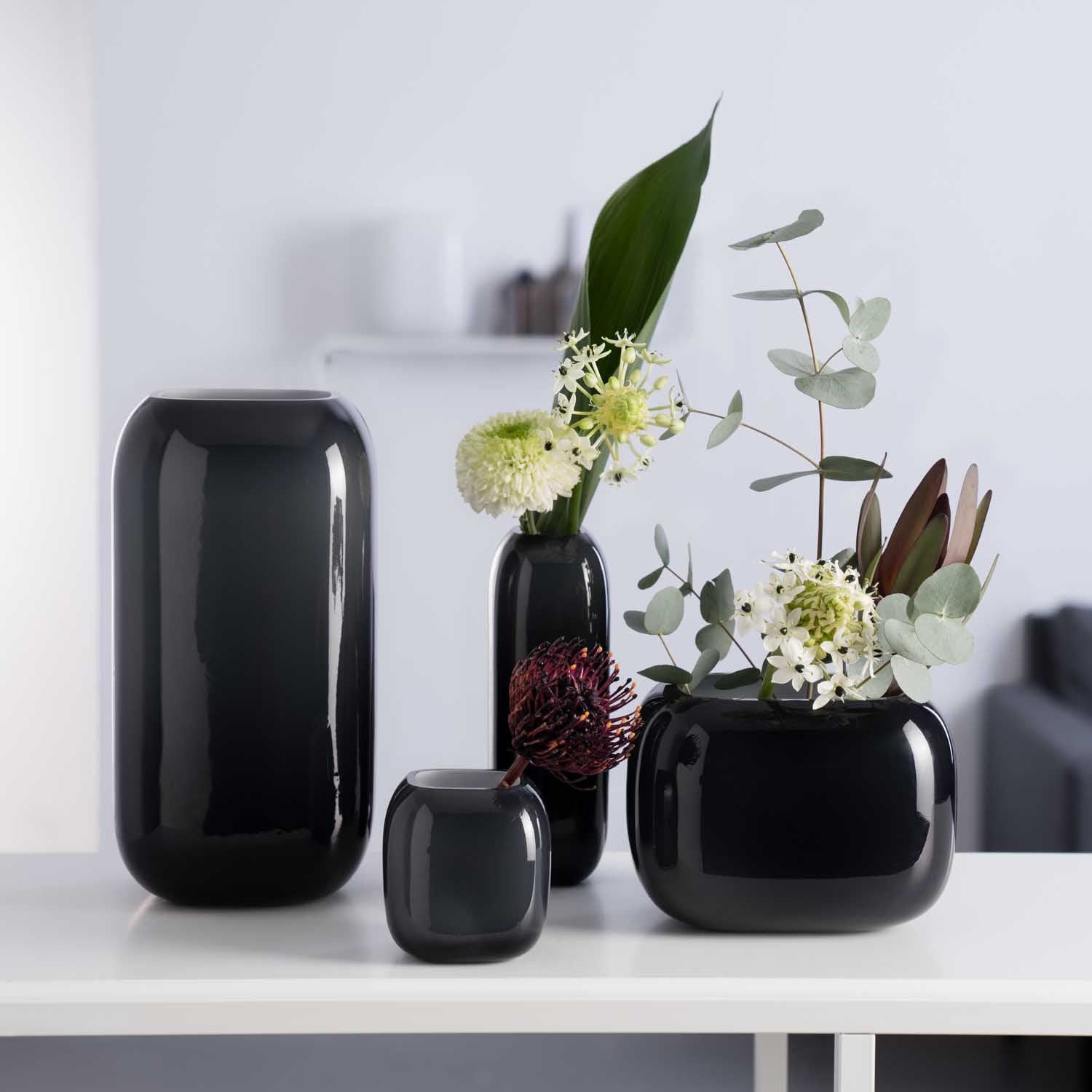 Schwarze Glasvasen der Serie MILANO in verschiedenen Groessen mit Blumenarrangement auf weissem Regal