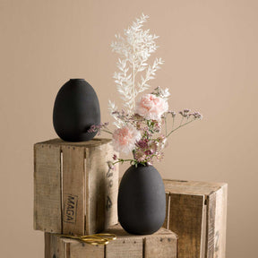 Schwarze Metallvase CASOLARE auf Holzkisten mit Blumenstrauss arrangiert