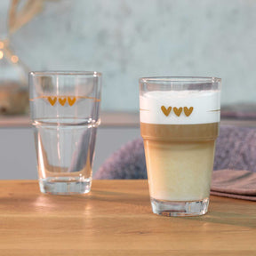 Zwei Becher SOLO mit Herz-Gravur auf Holztisch, einer mit Wasser, einer mit Latte Macchiato