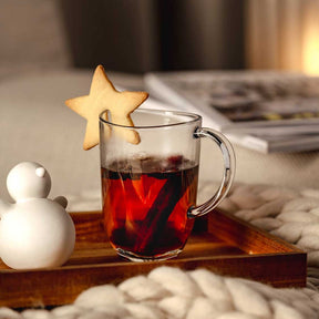 Glastasse SILENZIO mit rotem Tee, Stern-Deko und weißen Weihnachtsfiguren auf Holzablage