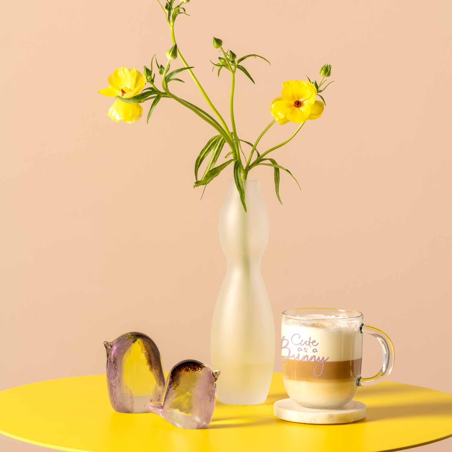 Glasvogel VIVACE mit gelben Blumen und Kaffeetasse auf gelbem Tisch