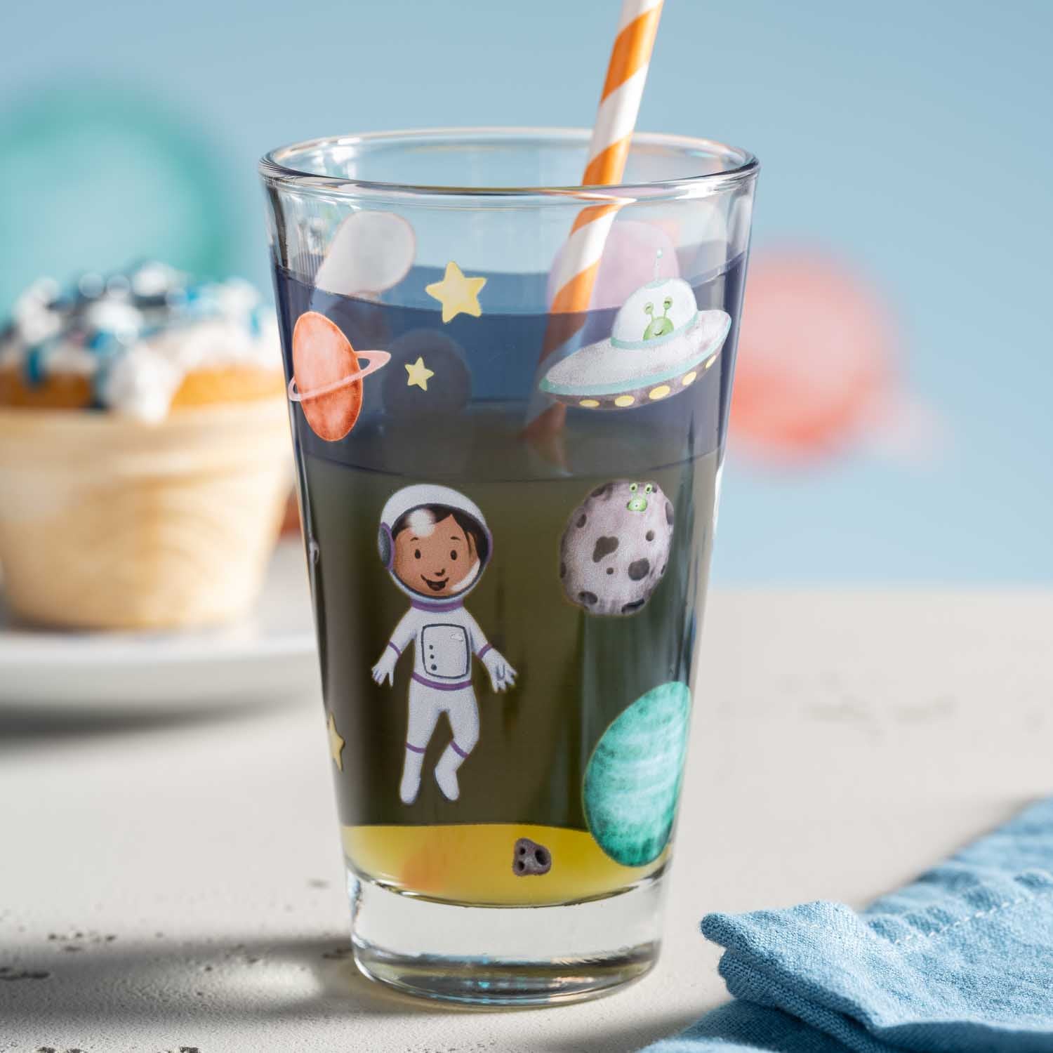 Trinkglas BAMBINI AVVENTURA mit Weltall-Motiven, Strohhalm, auf Tisch mit Deko