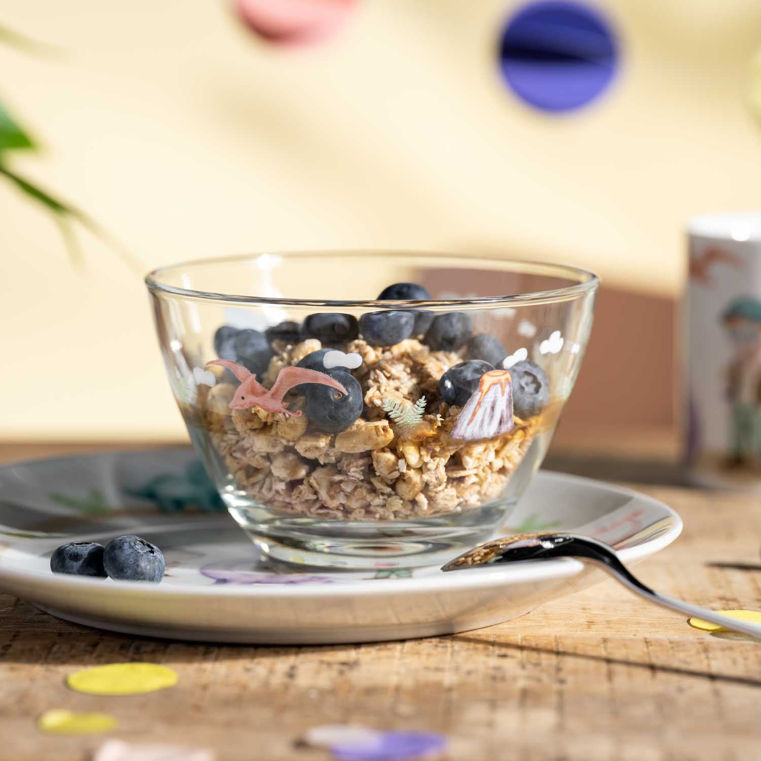 Glasschale mit Müsli, Blaubeeren und Löffel auf Teller, Tischdeko