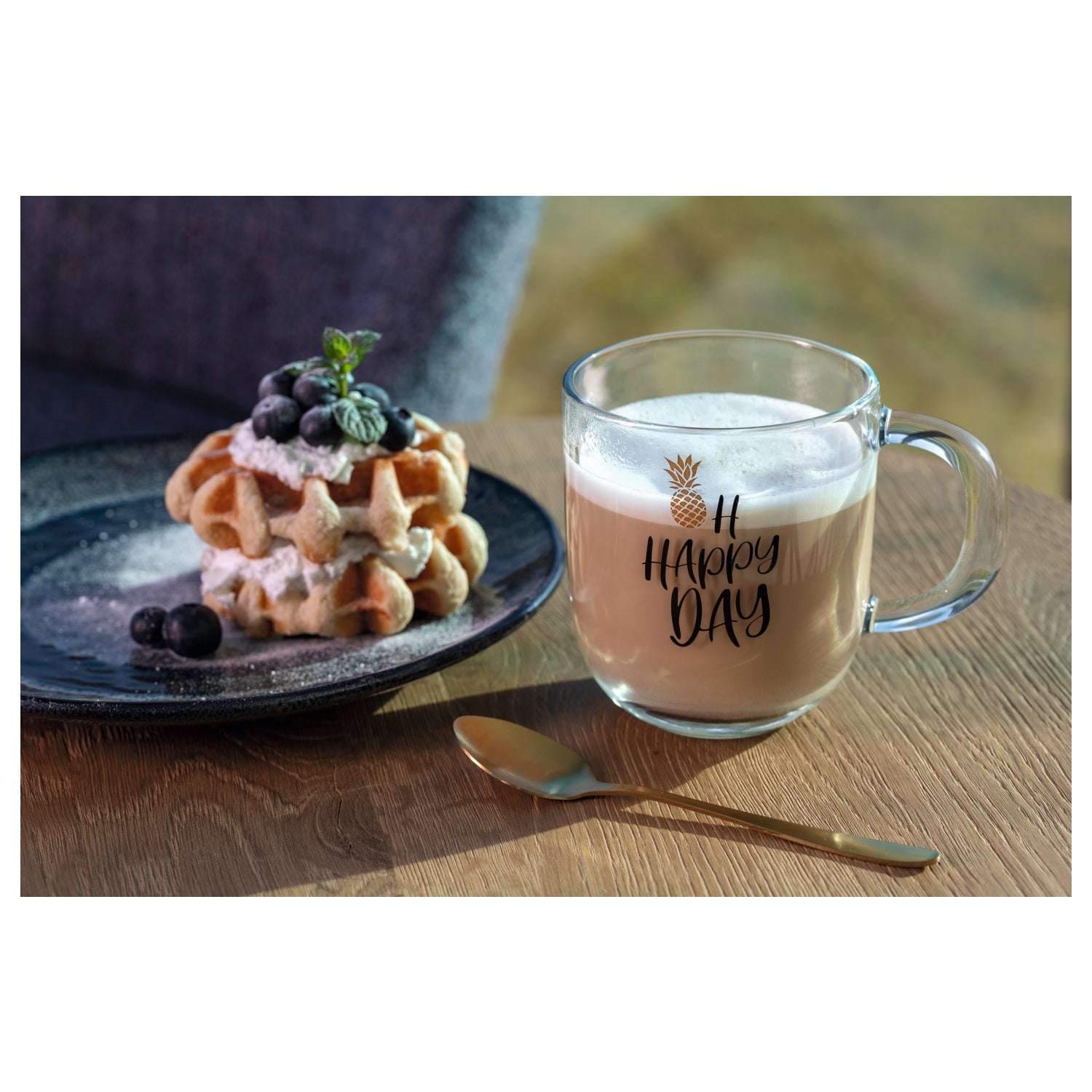 Tasse EMOZIONE mit "OH HAPPY DAY" Schriftzug auf Holztisch, daneben Waffel mit Beeren auf Teller