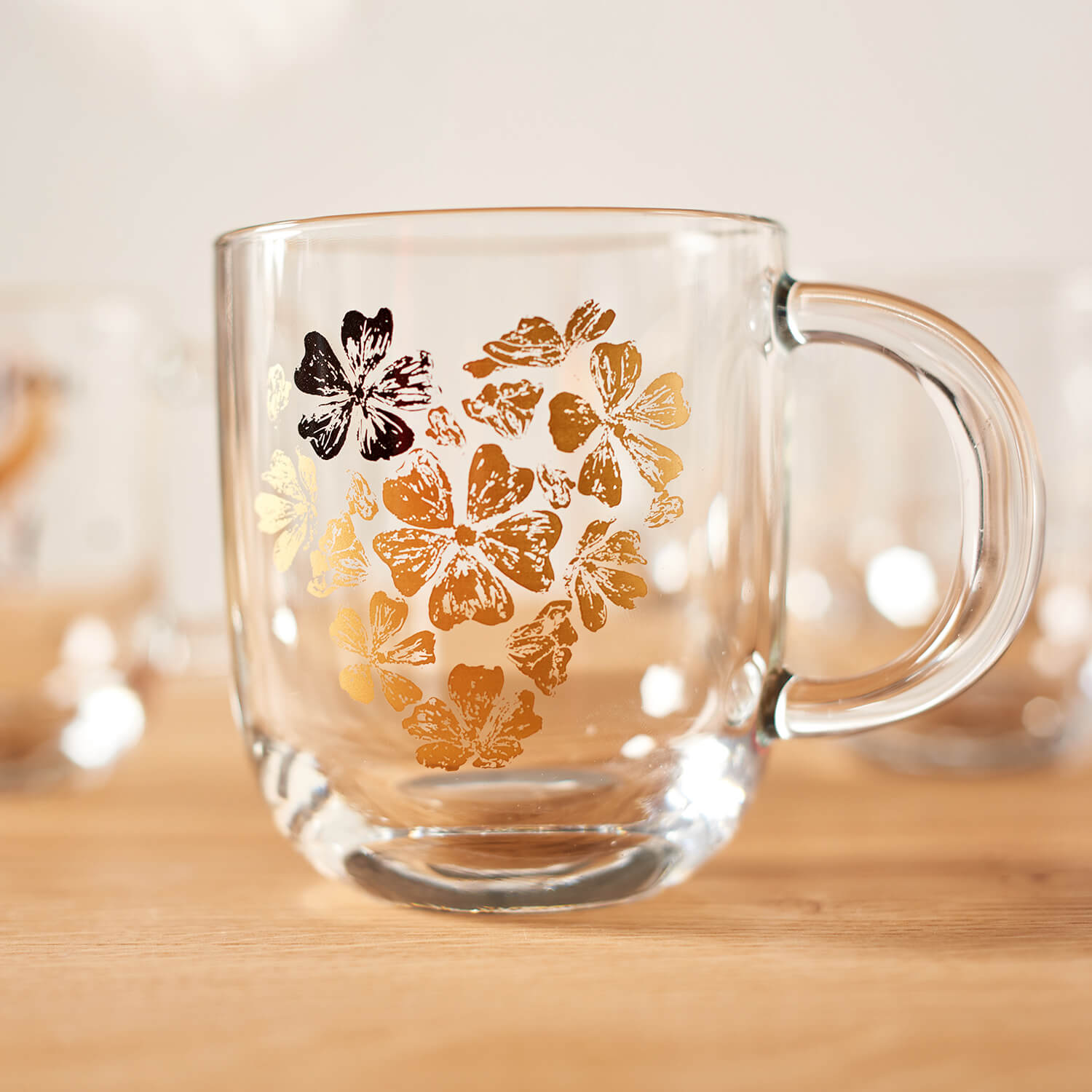 Tasse EMOZIONE mit goldenem Blumenherz-Motiv auf Holztisch