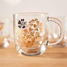 Tasse EMOZIONE mit goldenem Blumenherz-Motiv auf Holztisch