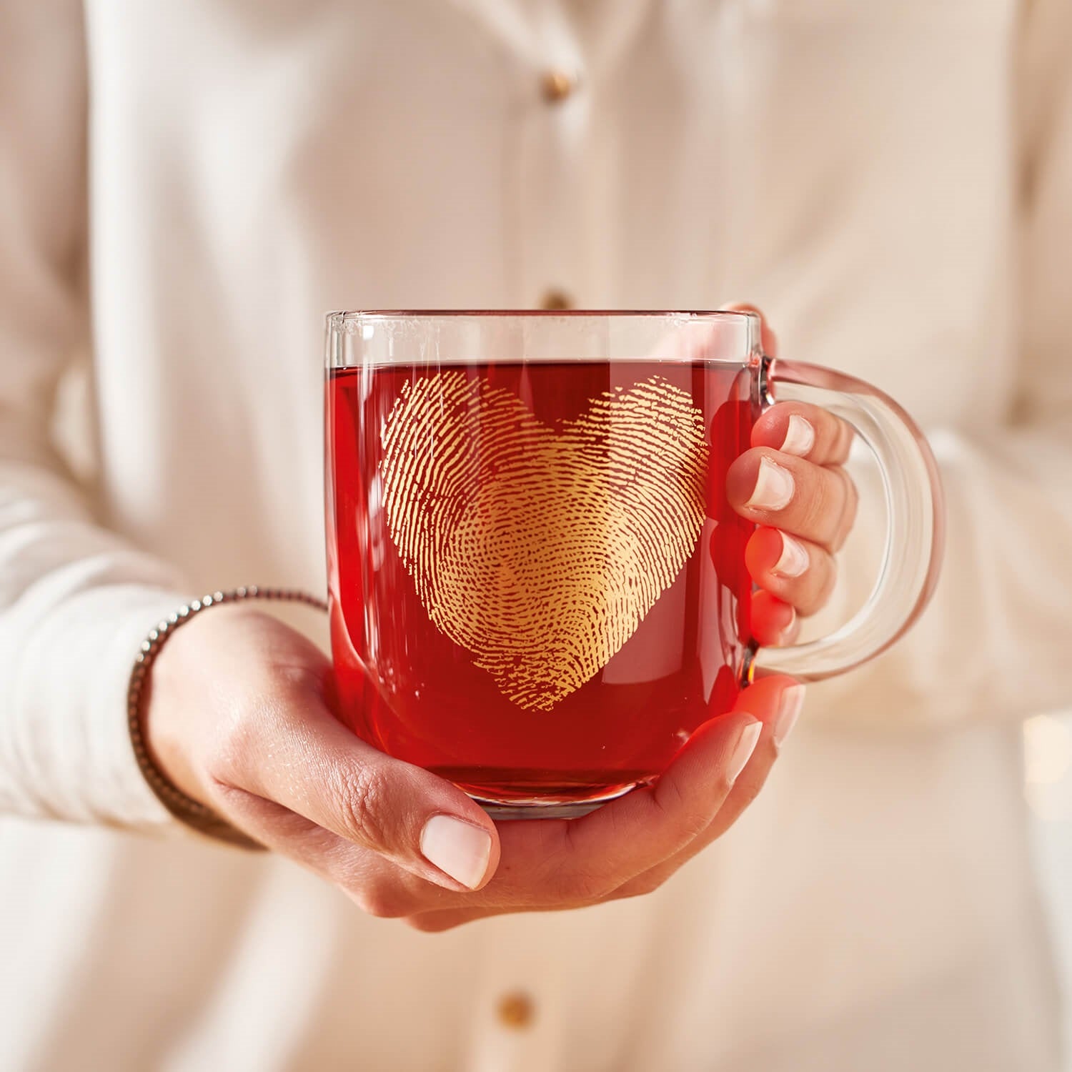 Tasse EMOZIONE 400 ml mit goldenem Fingerabdruck-Herz-Motiv, gefüllt mit rotem Tee, in Frauenhand