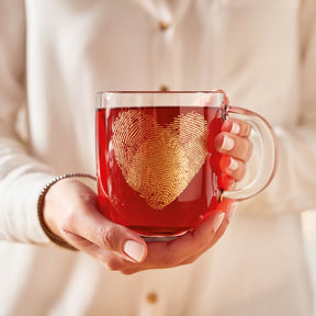Tasse EMOZIONE 400 ml mit goldenem Fingerabdruck-Herz-Motiv, gefüllt mit rotem Tee, in Frauenhand