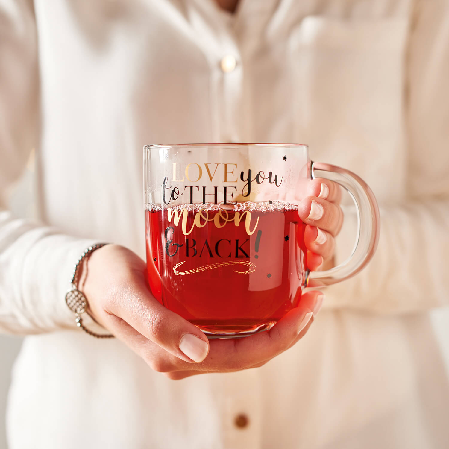 Tasse EMOZIONE mit rotem Inhalt, von einer Person in weißer Kleidung gehalten