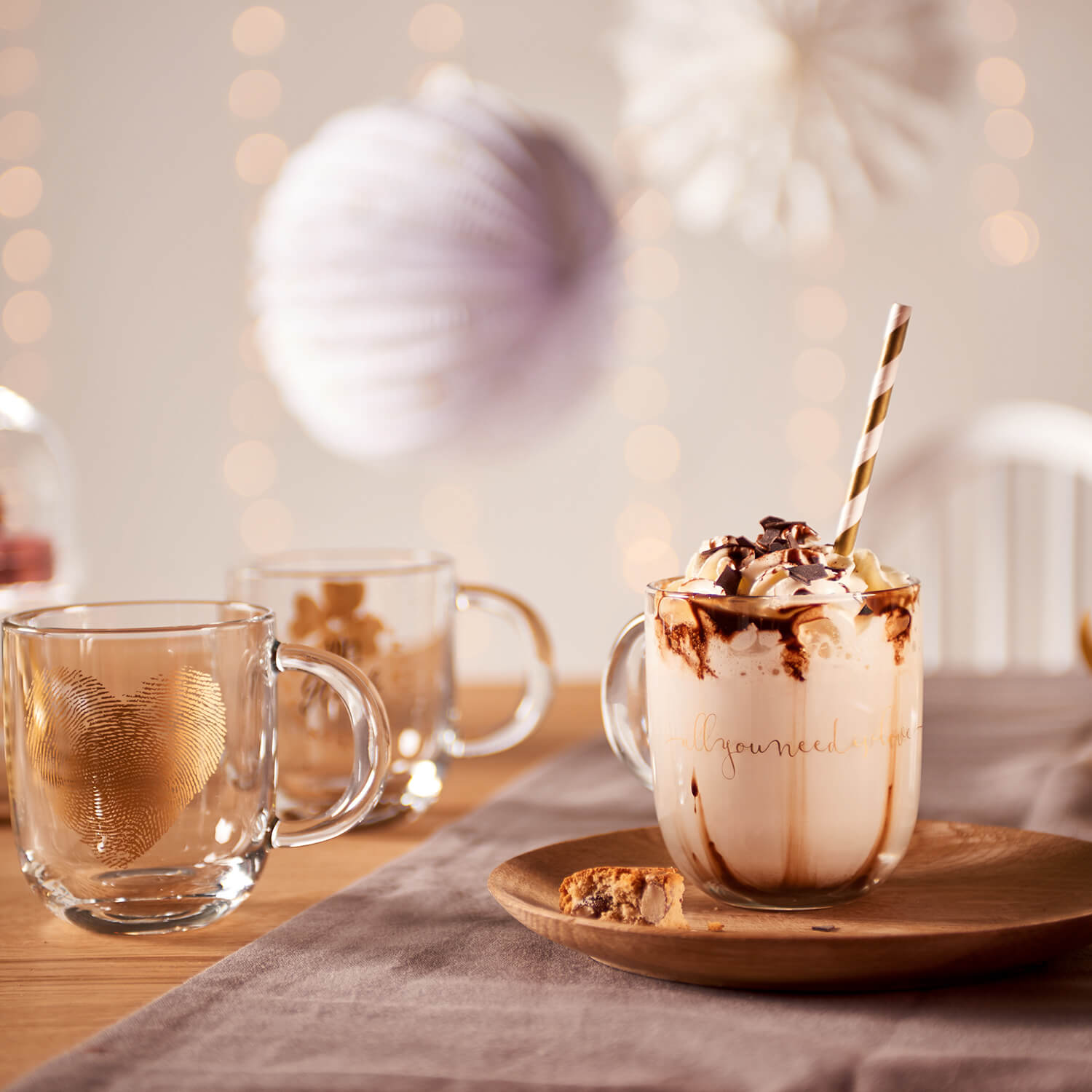 Tasse EMOZIONE mit Kakao und Schokoflocken auf Holztablett, Tische mit Gläsern und Dekoration