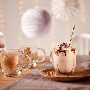 Tasse EMOZIONE mit Kakao und Schokoflocken auf Holztablett, Tische mit Gläsern und Dekoration