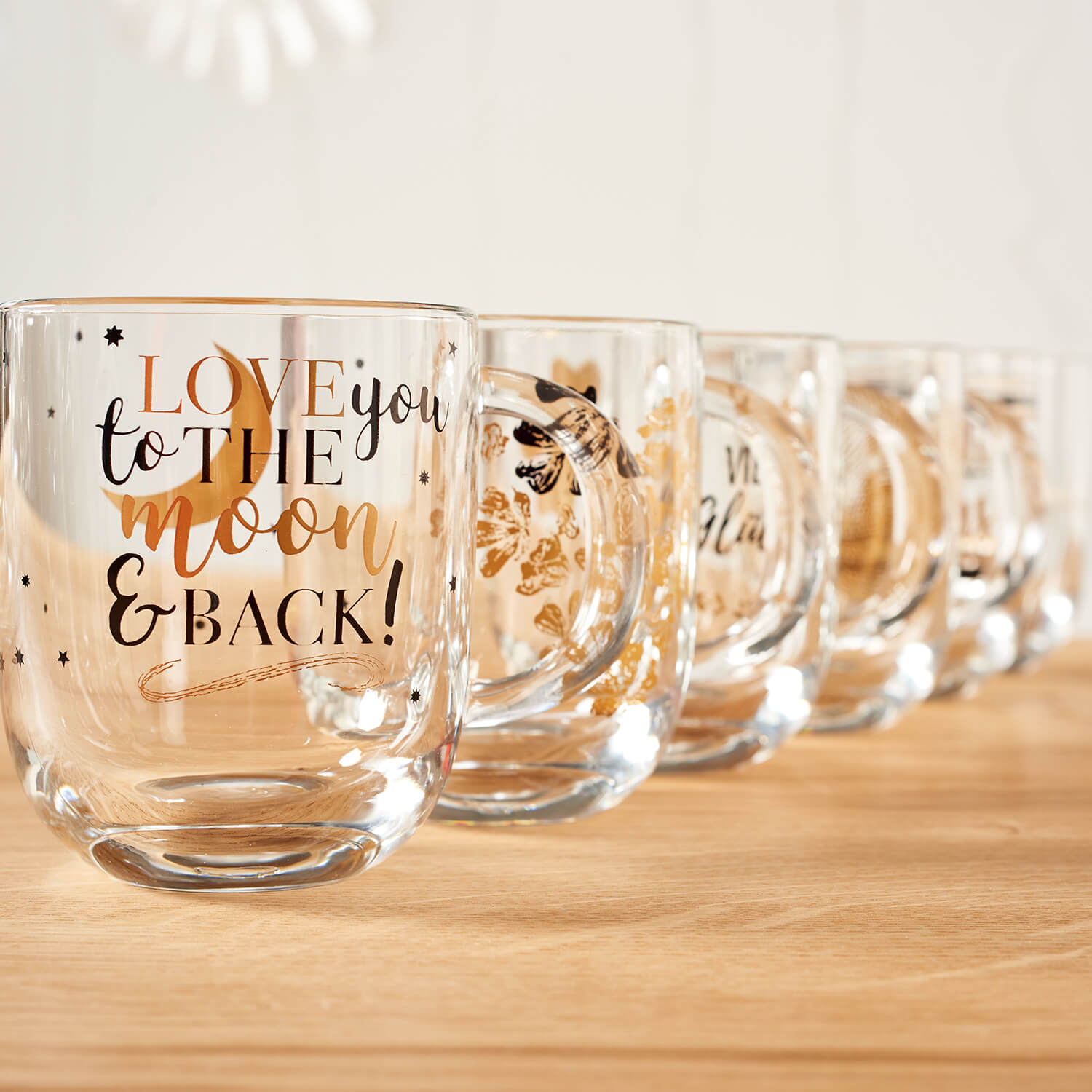 Mehrere Glaeser in Reihe auf Holzflaeche, vorderstes mit Gravur "LOVE you to the MOON & BACK
