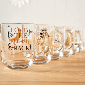 Mehrere Glaeser in Reihe auf Holzflaeche, vorderstes mit Gravur "LOVE you to the MOON & BACK