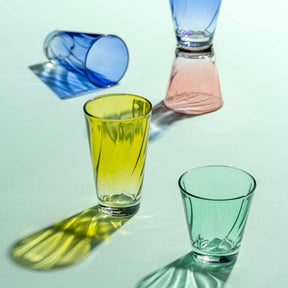 Farbige Gläser in Blau, Gelb, Rosa und Grün mit Schatten auf weißem Untergrund