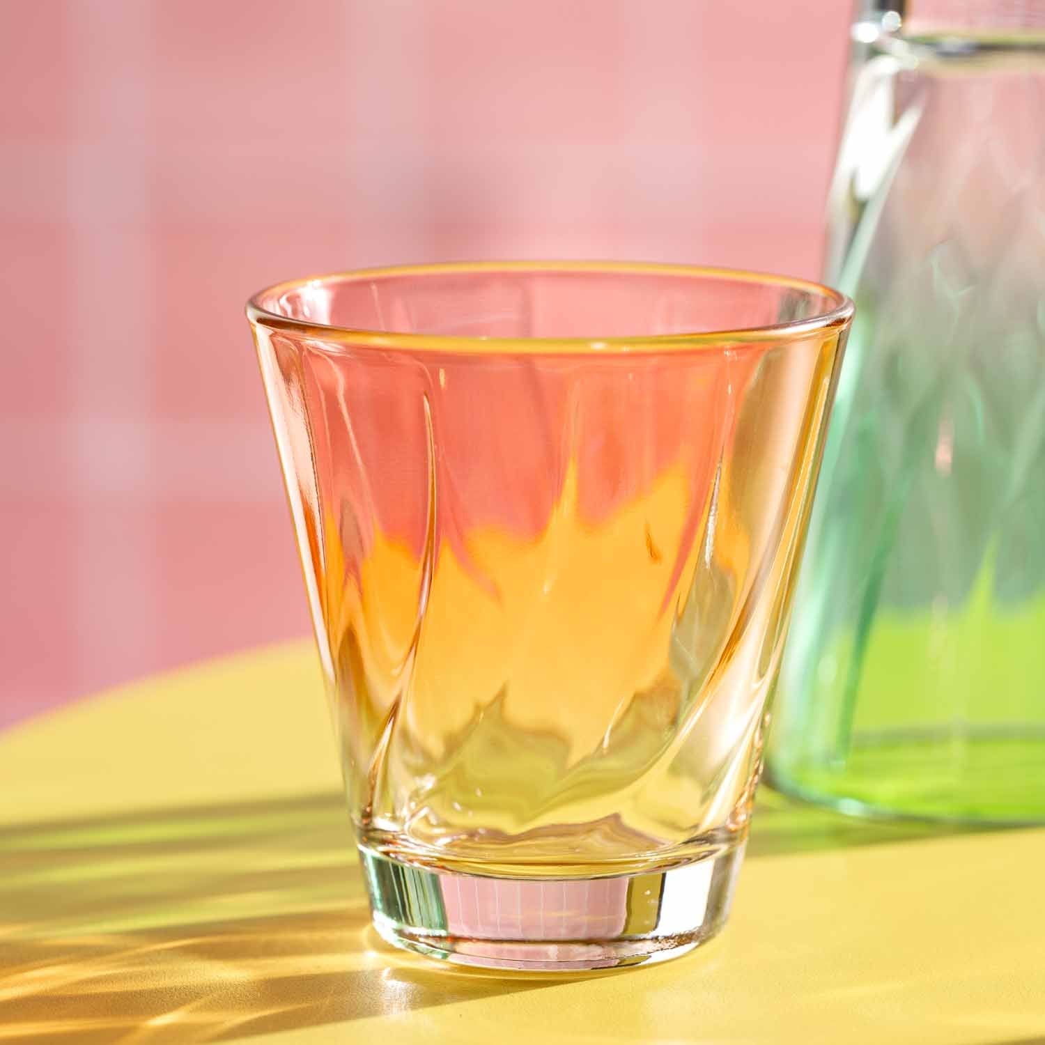 Trinkglas TWIST mit gelblicher Flüssigkeit auf gelblichem Untergrund, rosa Hintergrund