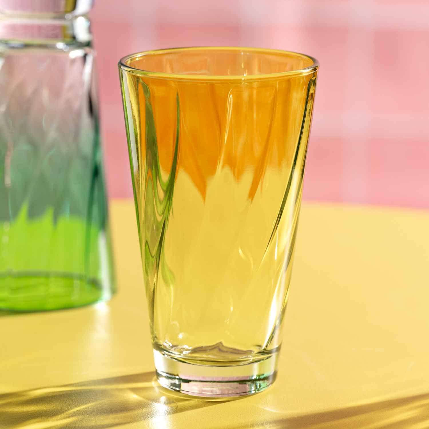 Trinkglas TWIST 300 ml gelb auf gelblicher Oberfläche, daneben Glasflasche