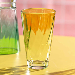 Trinkglas TWIST 300 ml gelb auf gelblicher Oberfläche, daneben Glasflasche