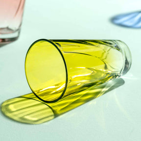 Gelbes Trinkglas TWIST umgekippt auf weißer Oberfläche mit Flüssigkeit